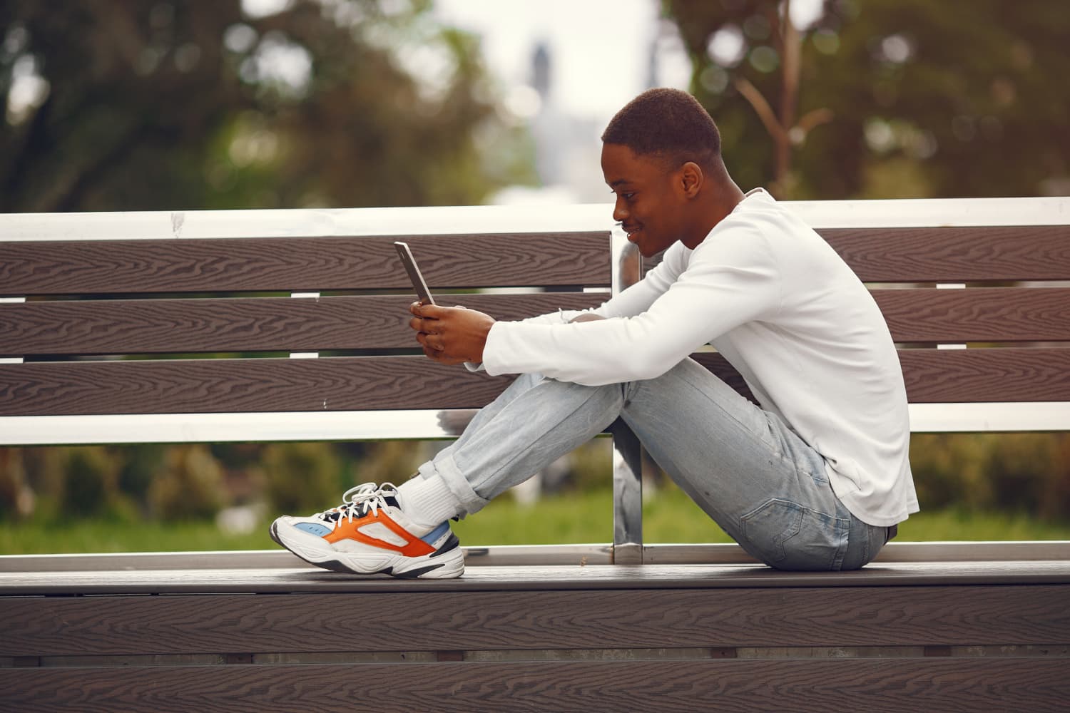 Young man sitting on a bench, smiling at his phone